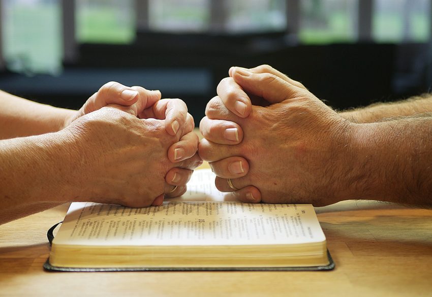 hands resting on bible, people praying